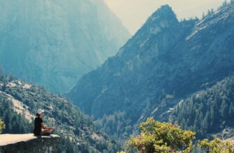 A woman practices meditation on a cliff edge, surrounded by majestic mountains and serene nature.